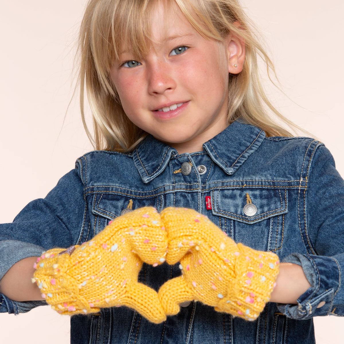 Yellow speckled knit mittens with scalloped cuffs, worn on hands