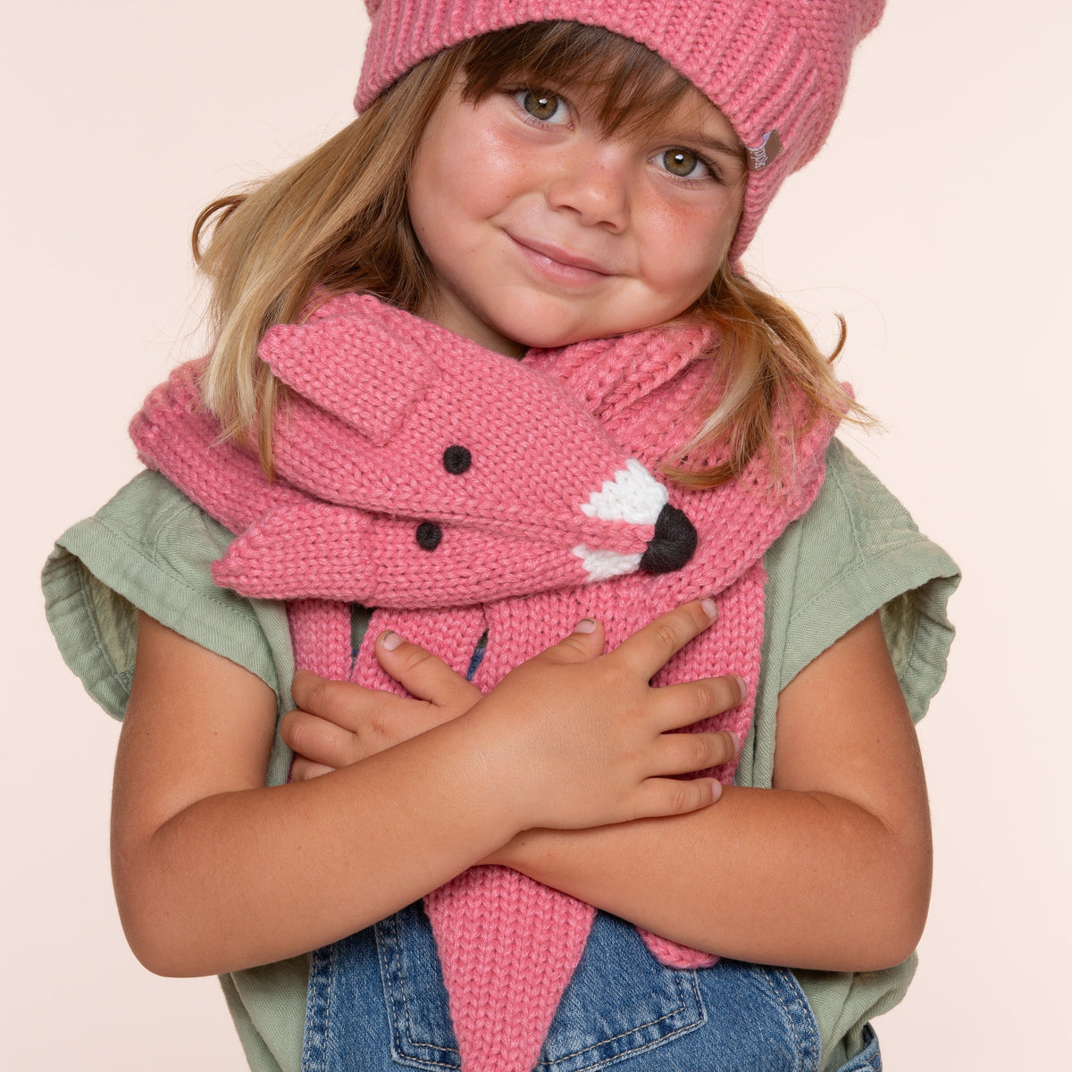 Child wearing a pink knitted fox scarf wrapped around the neck, with the fox face at the front.