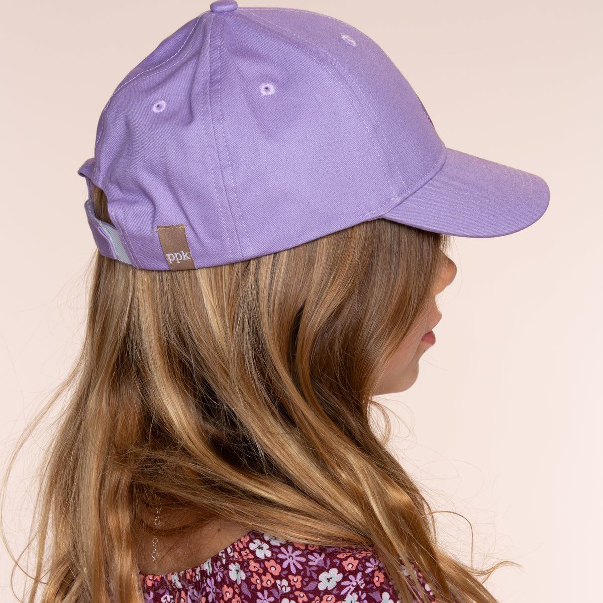 Side view of the purple baseball cap worn by a child, with an adjustable back strap