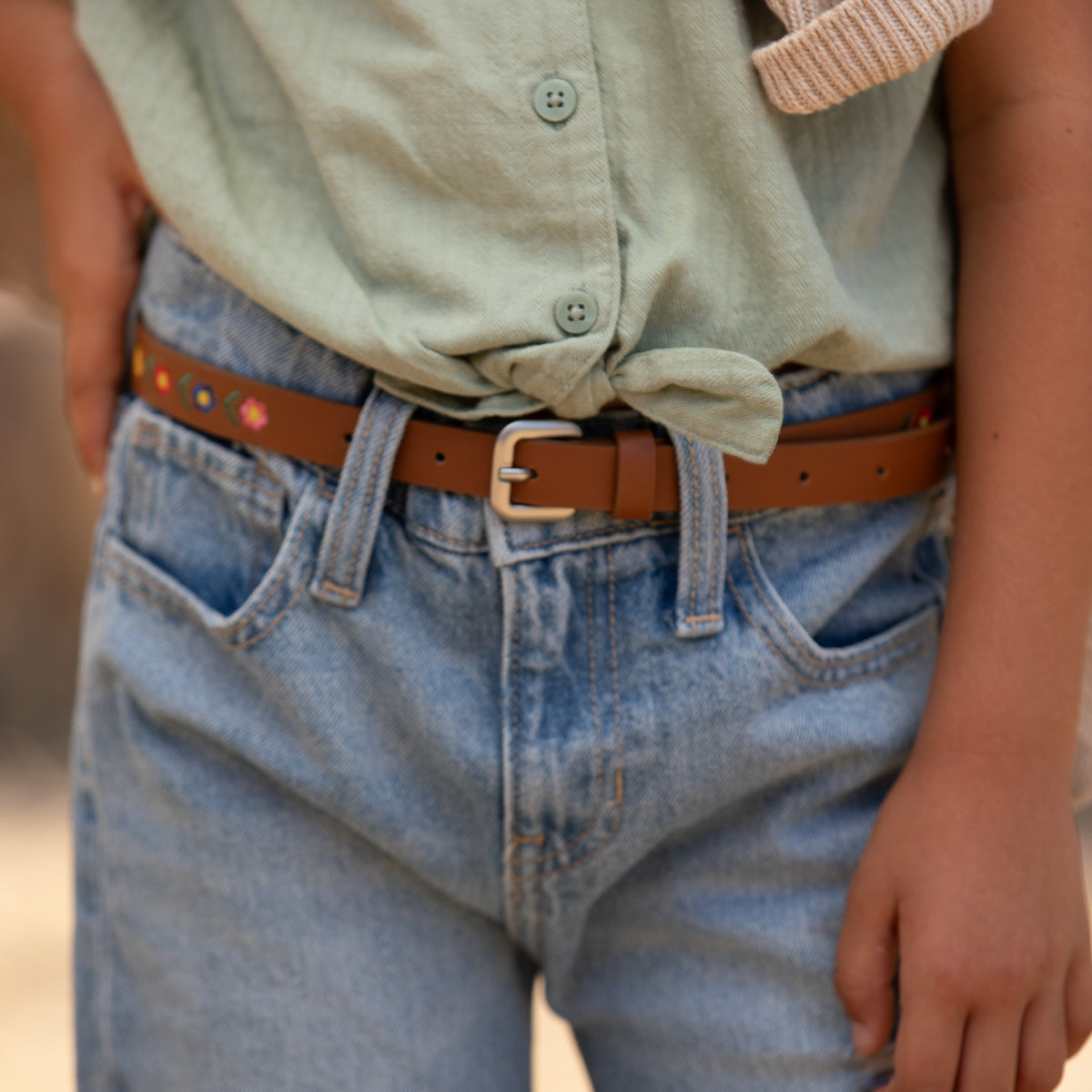 Brown floral-embroidered belt worn with jeans, showing its buckle and strap