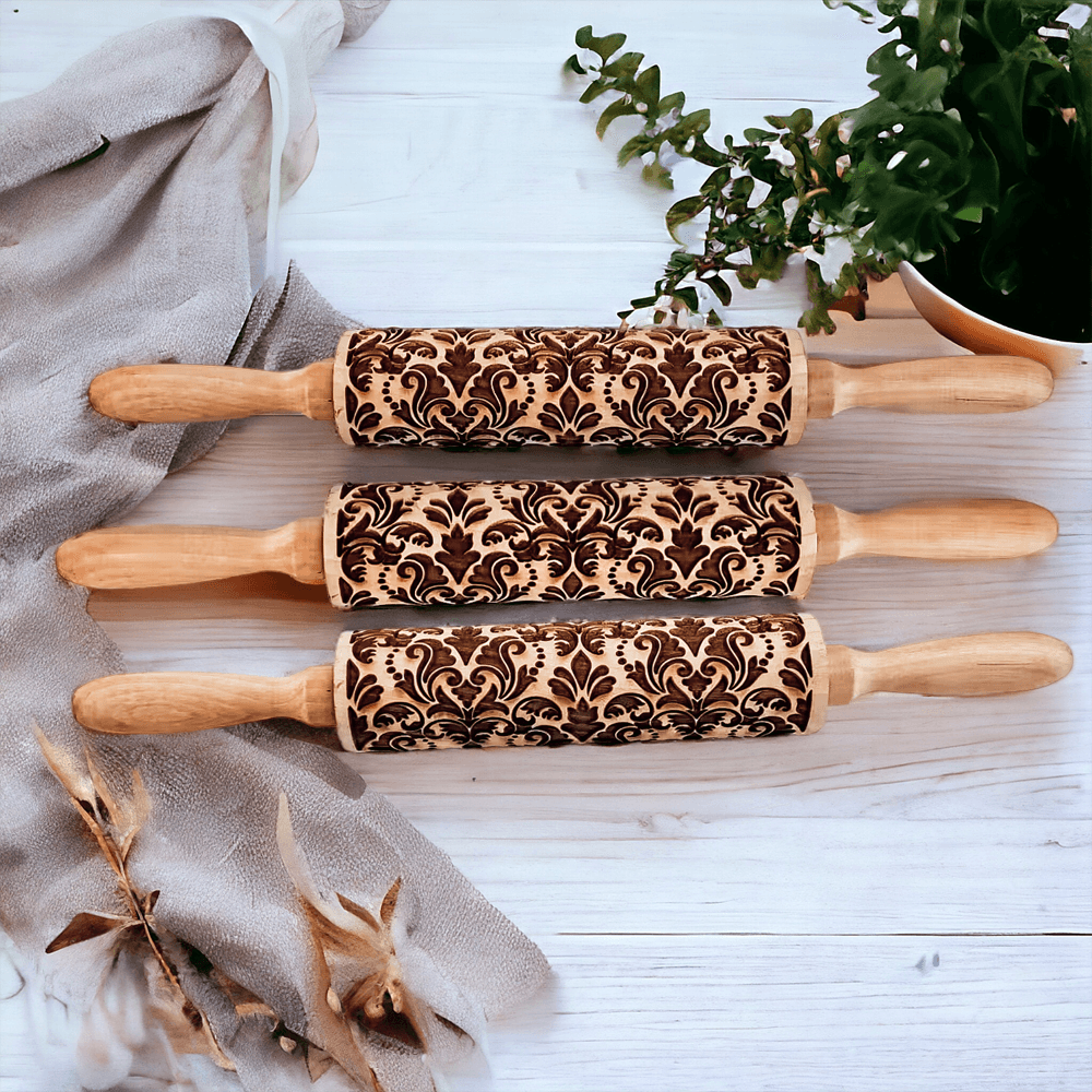 Three embossed wood rolling pins with ornate brown damask patterns on a light table