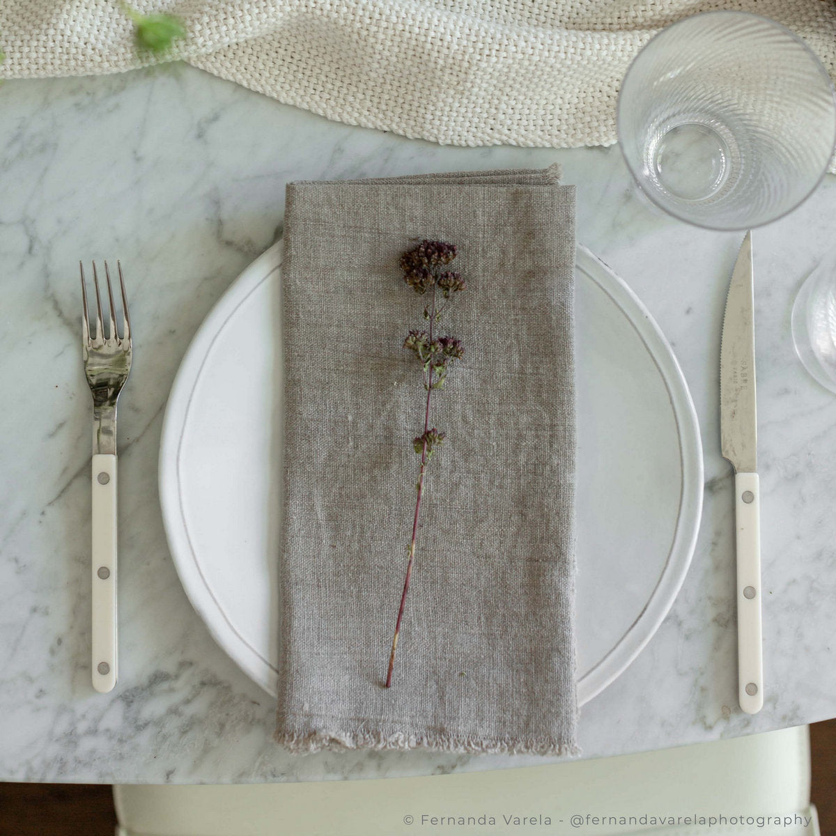 Grey linen napkin with small floral sprig, frayed hem, folded over plate