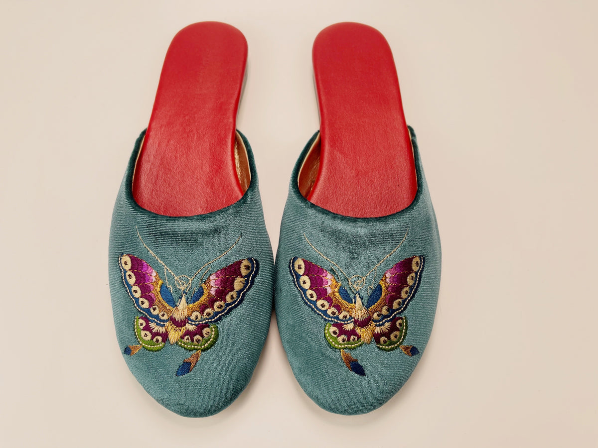 Pair of teal velvet mule slippers with butterfly embroidery and red insoles