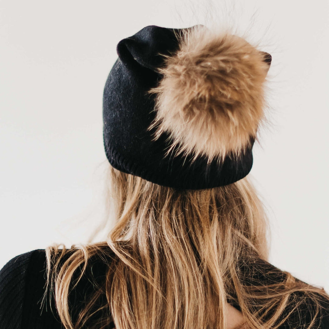 Black knit beanie shown from the back, with a large tan fur pom