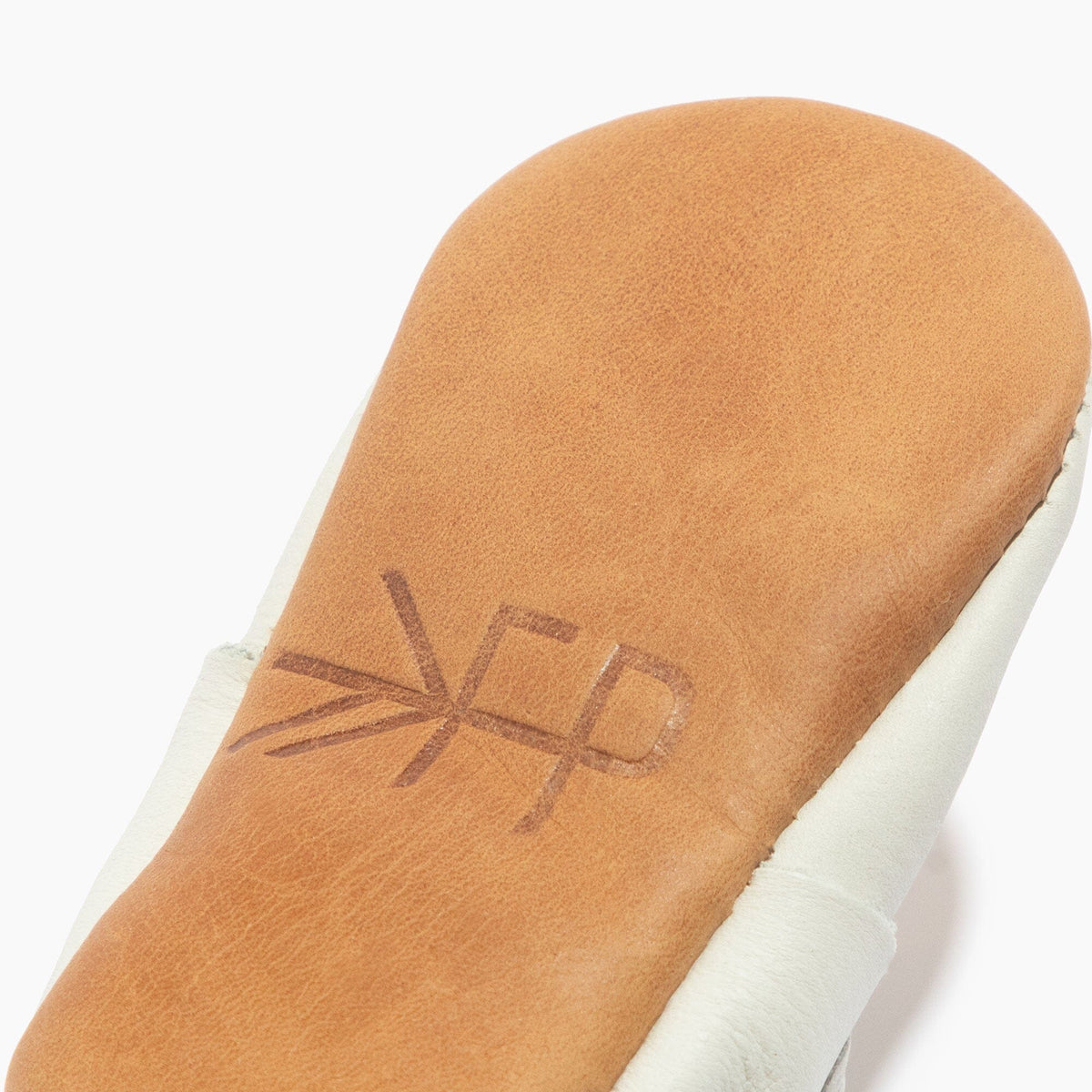 White baby shoe with tan suede outsole featuring molded logo detail