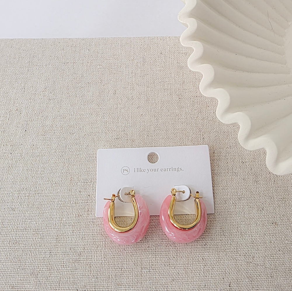 Pink resin hoop earrings with gold-tone hardware displayed on fabric background
