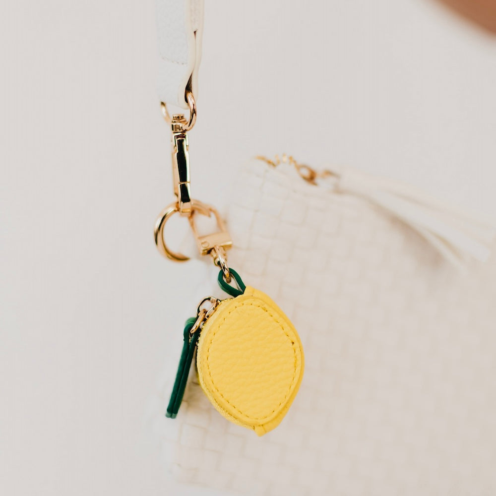 Lemon-shaped leather keychain charm with gold clasp and small green tassel.