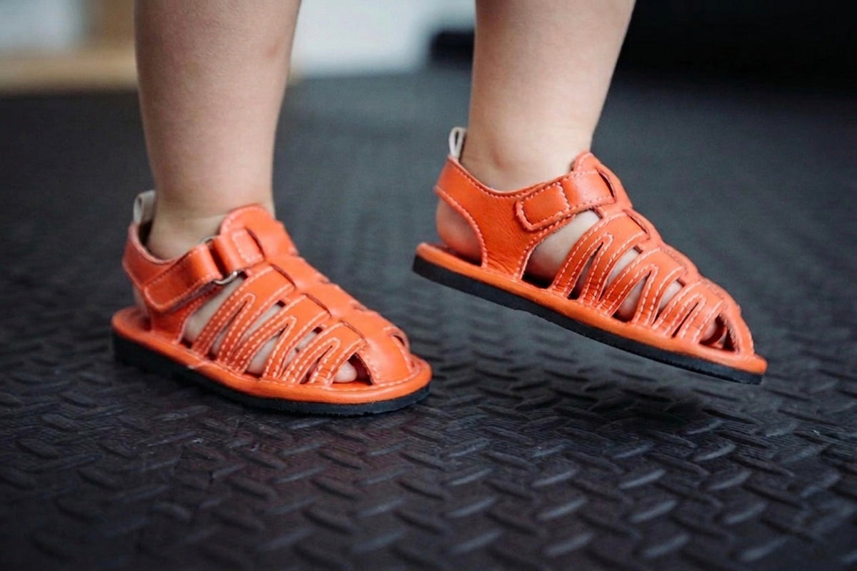 Pair of orange barefoot sandals with hook-and-loop straps and open-toe cutouts