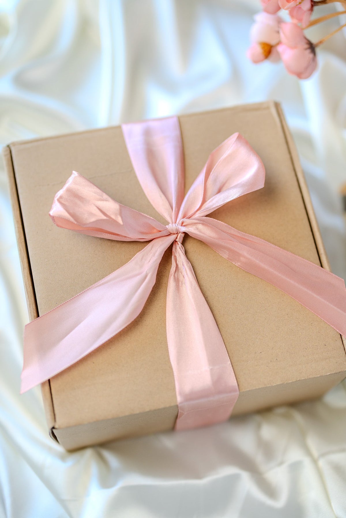Self-care gift box with pink satin ribbon bow on kraft cardboard packaging