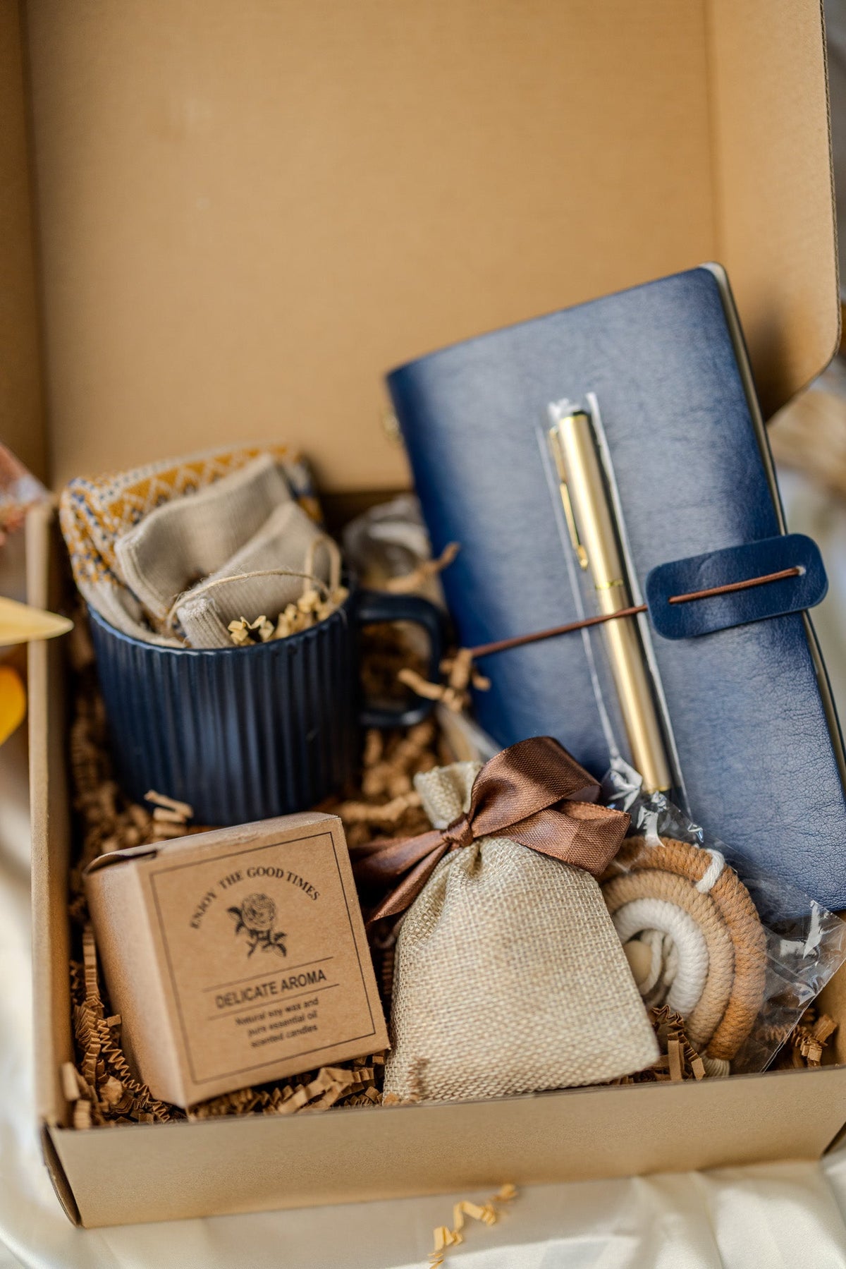 Full gift box view with blue notebook, gold pen, navy mug, candle and fabric pouch