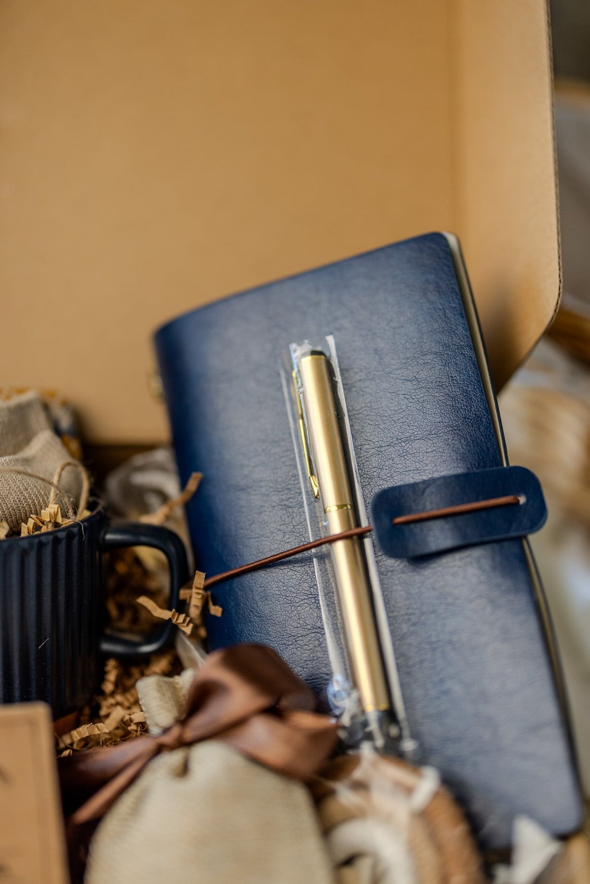 Gift box contents: blue notebook with leather strap, gold pen, navy mug, and pouch