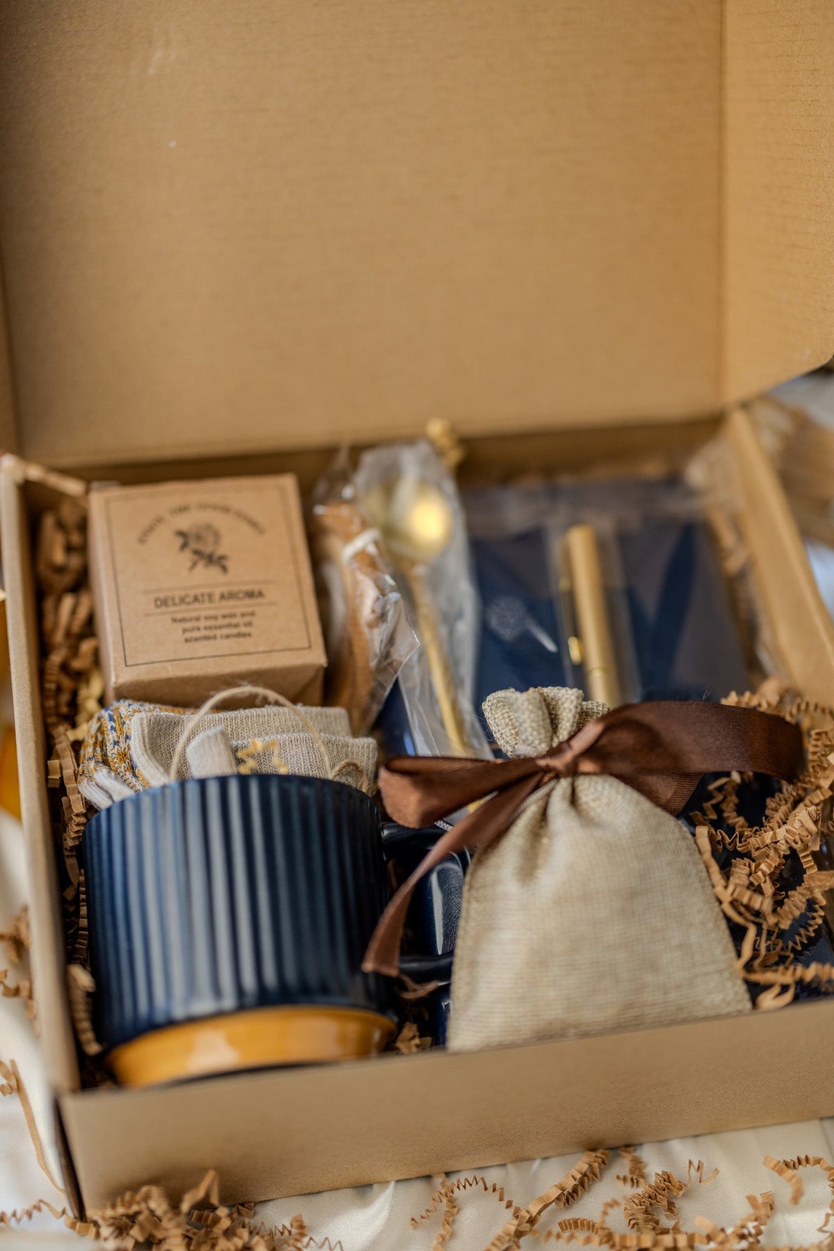 Gift box open with navy mug, beige drawstring pouch, and blue notebook with gold pen