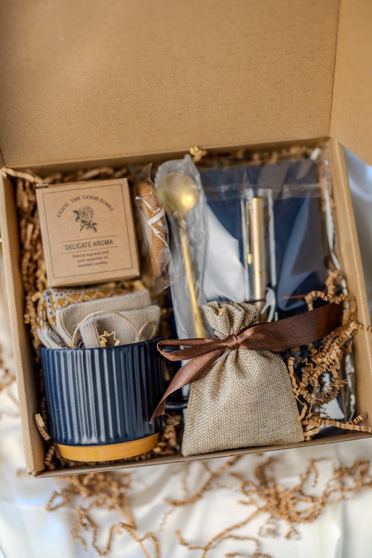 Gift box close-up with navy mug, blue notebook, gold pen, and beige pouch