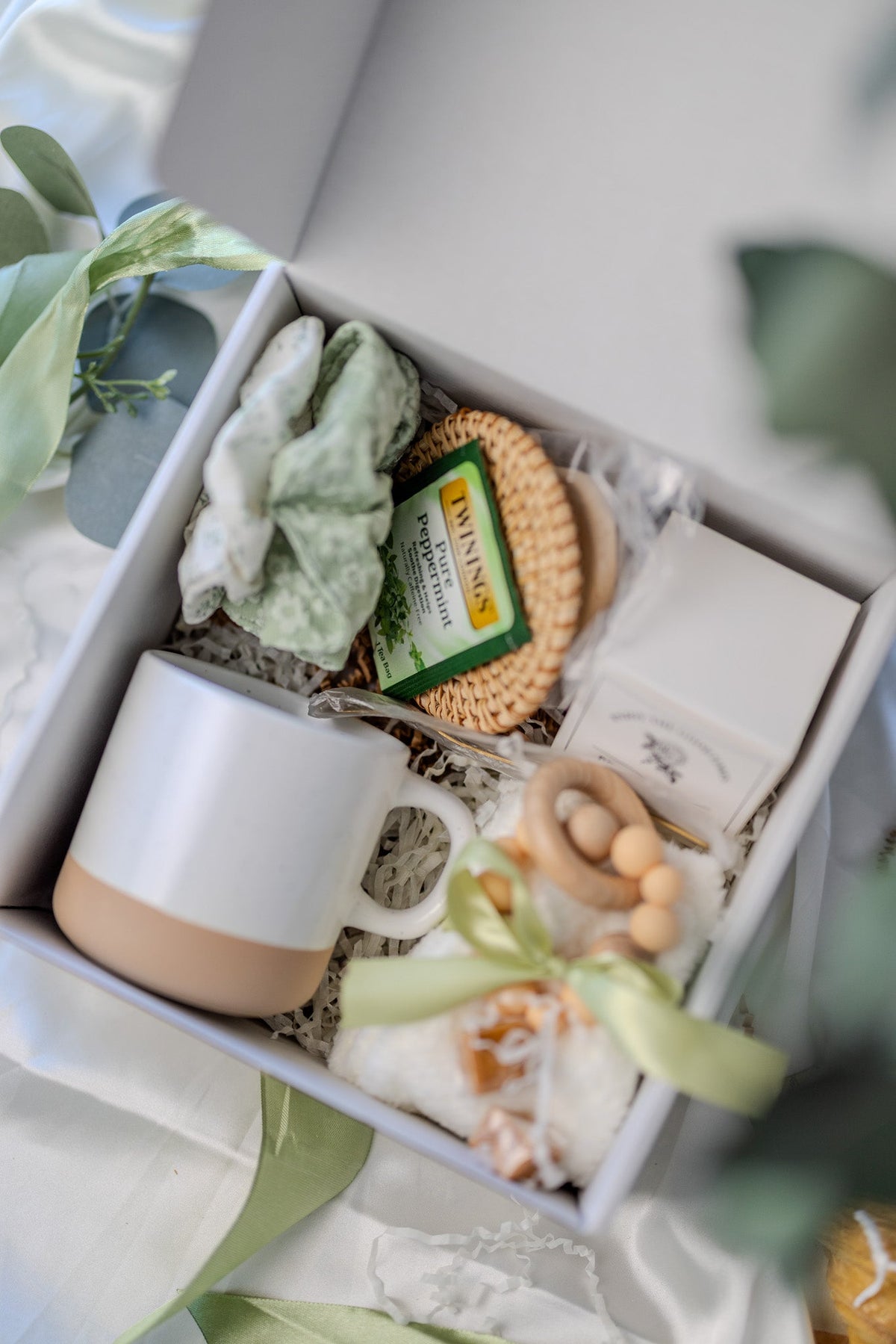 Self-care gift box with white mug, green soap, round woven sponge, and wooden bead soap