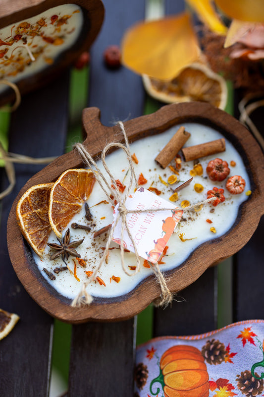Wooden pumpkin-shaped dough bowl candle with white wax and scattered autumn spices