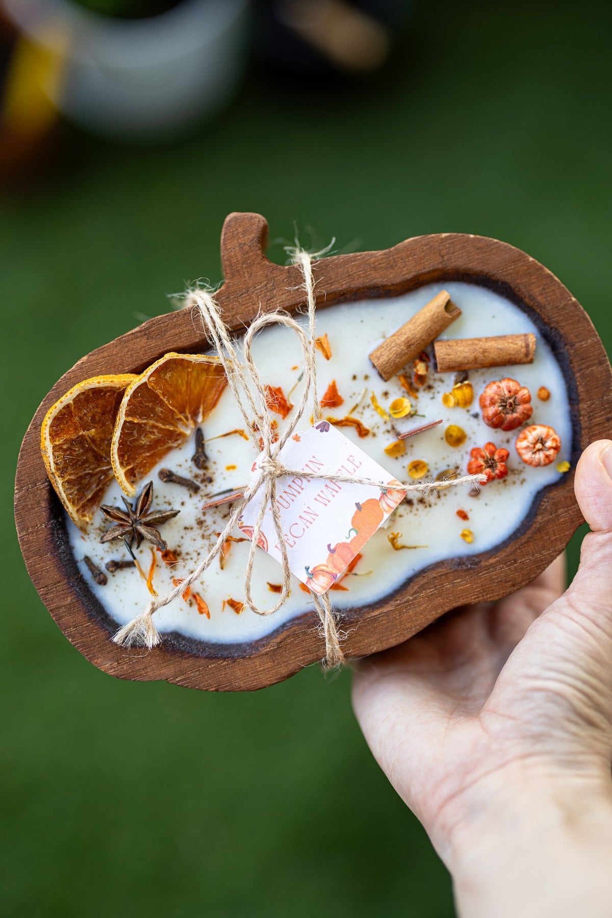 Wooden pumpkin-shaped dough bowl candle held in hand with cinnamon sticks and spice pieces