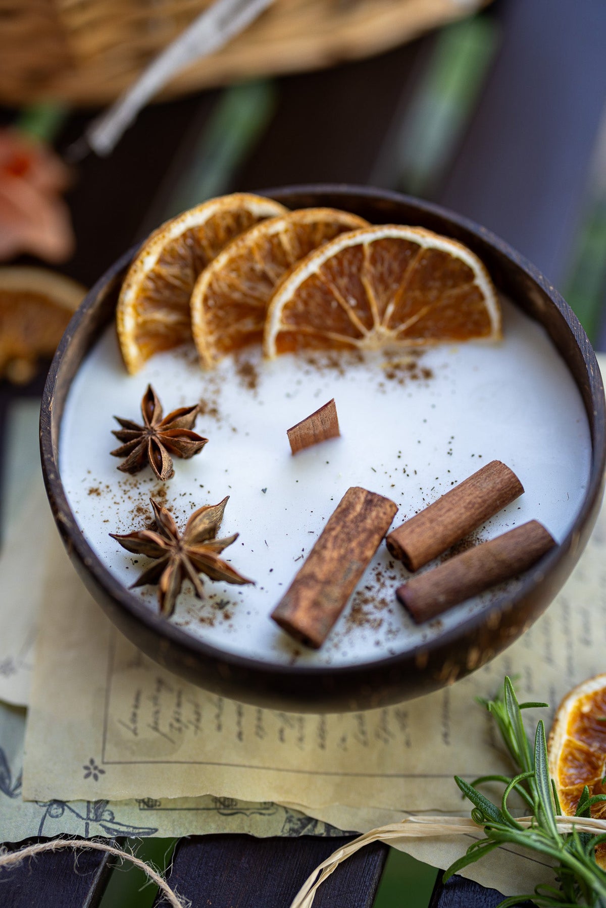 Coconut candle bowl featuring white wax topped with orange slices, cinnamon sticks, and star anise.