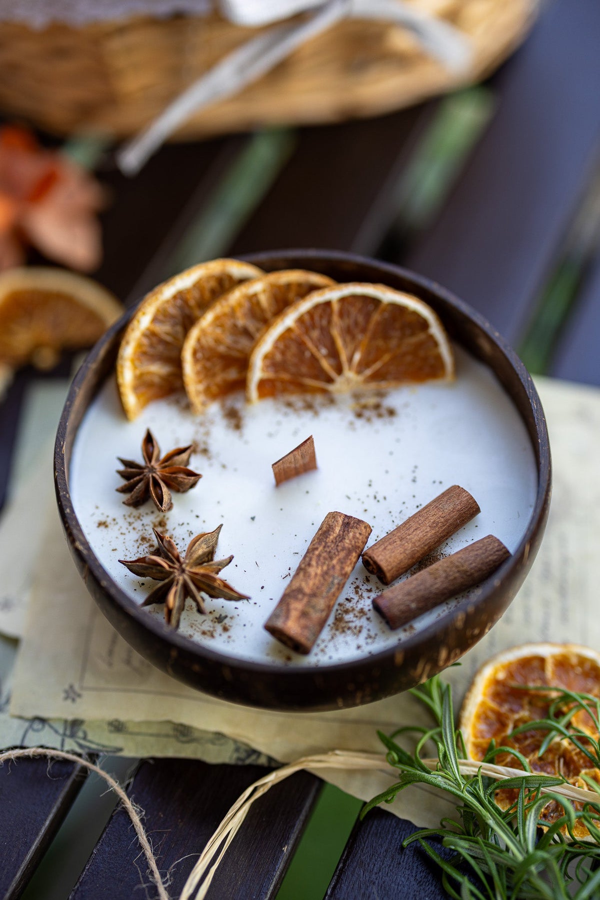 Coconut candle bowl on table with white wax, orange slices, cinnamon sticks, and star anise.