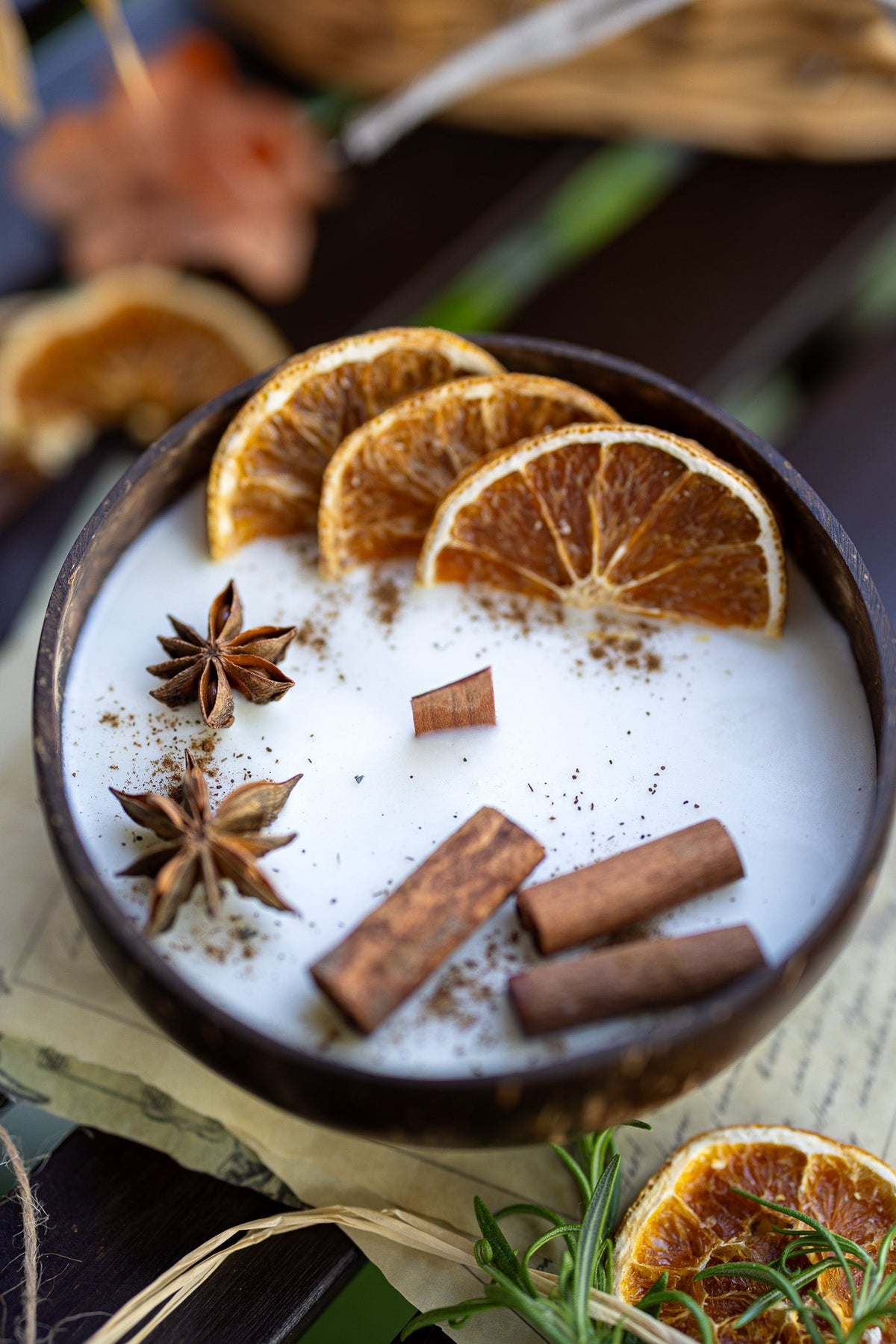 Coconut candle bowl close-up with white wax, orange slices, cinnamon sticks, and star anise.