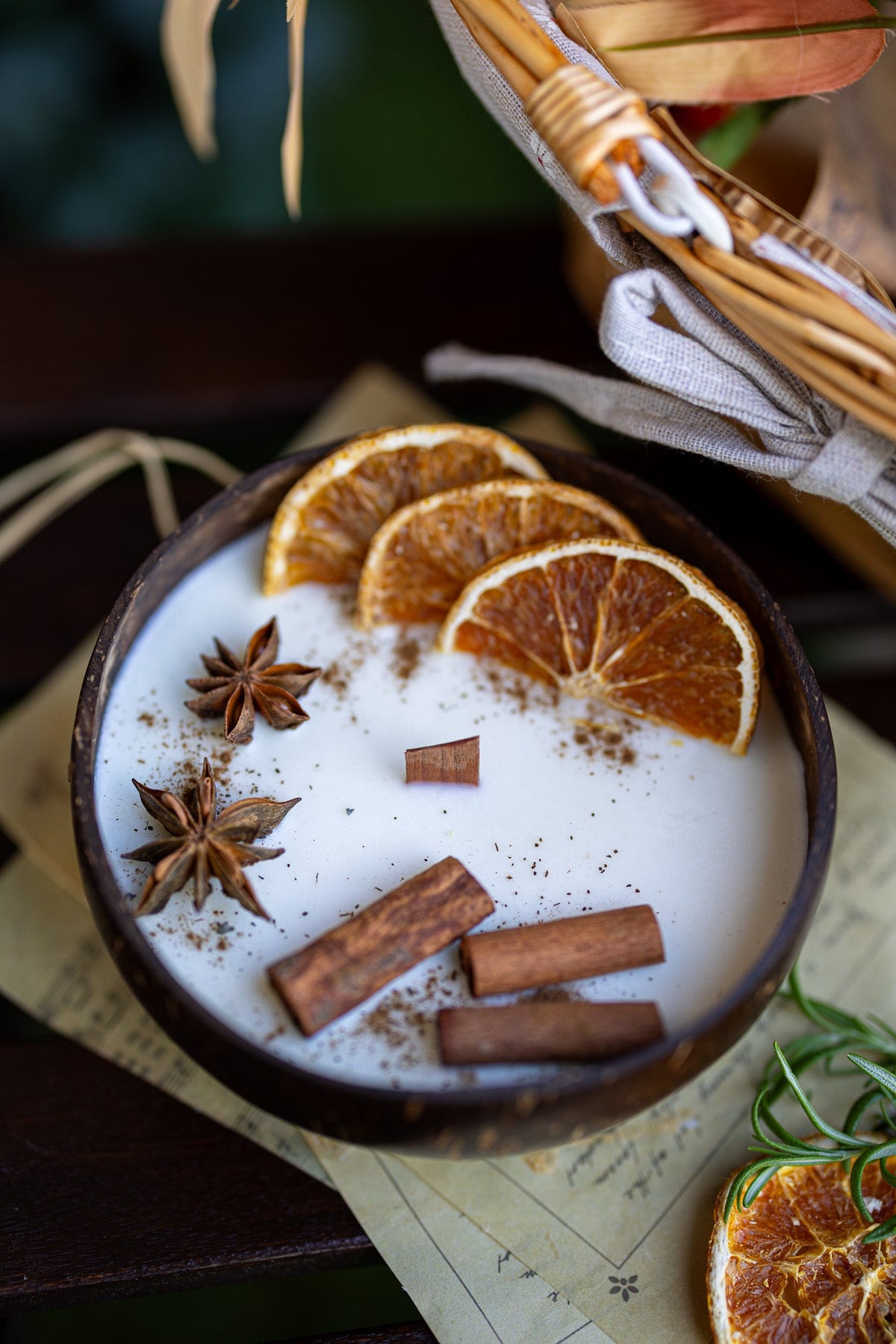 Coconut candle bowl with white wax, orange slices, cinnamon sticks, and star anise, angled view.