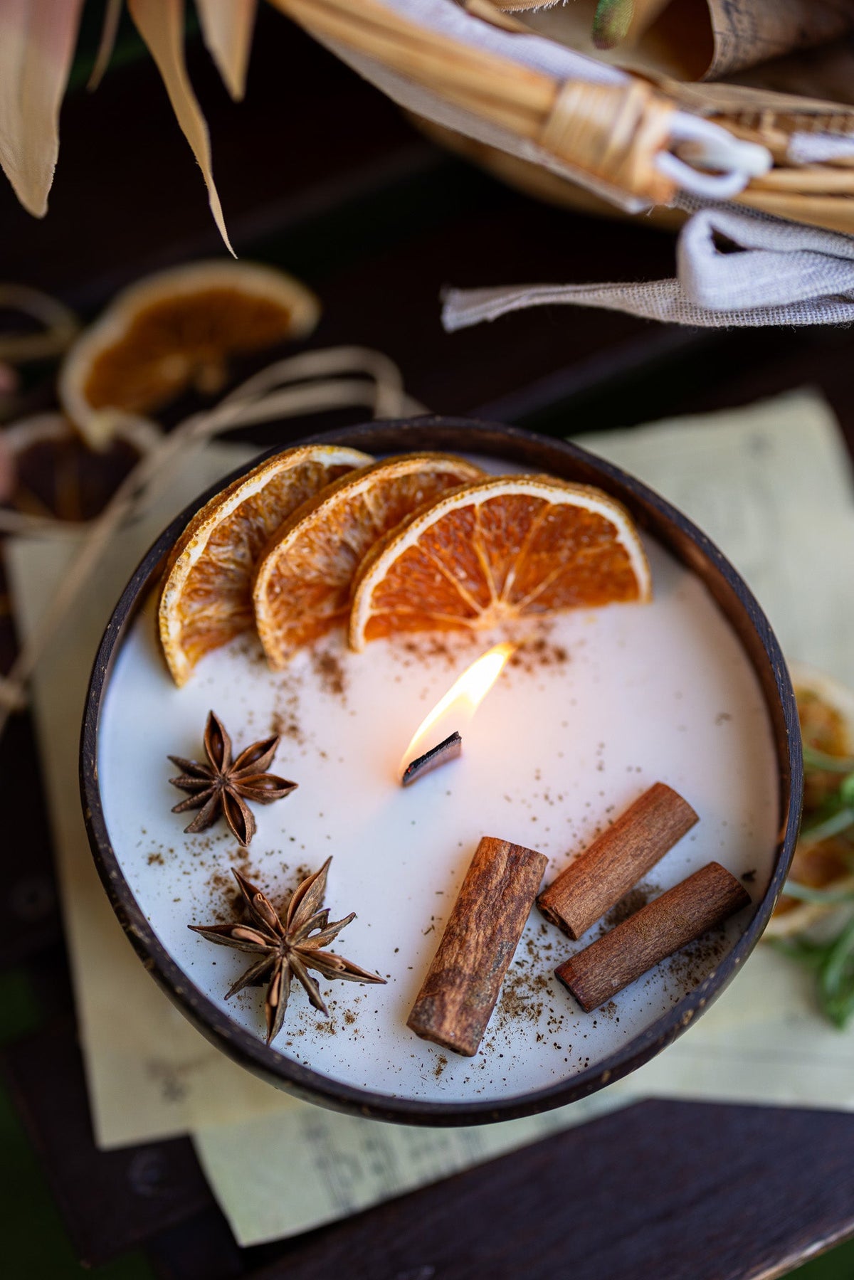 Coconut candle in dark bowl with orange slices, star anise, and cinnamon stick pieces