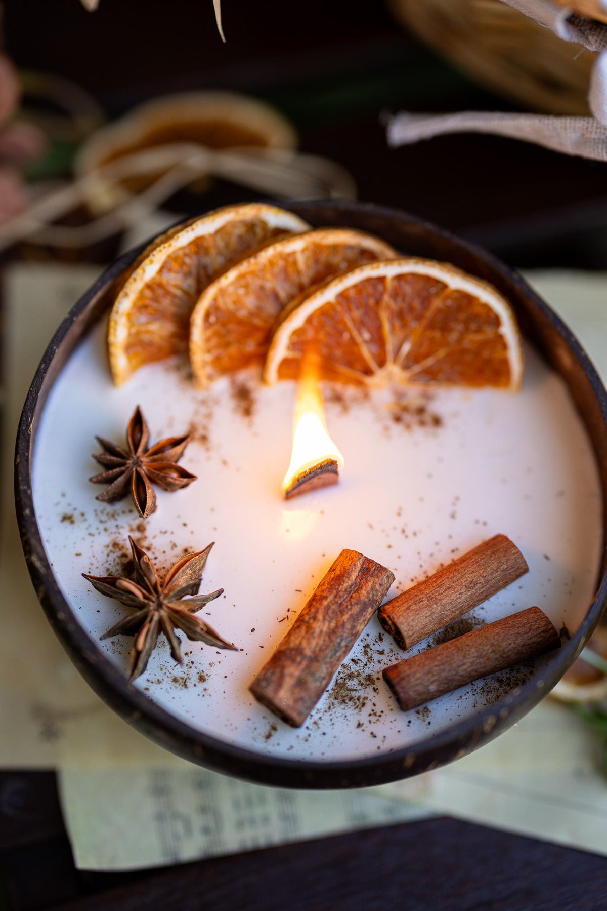 Coconut candle bowl with white wax, orange slices, cinnamon sticks, and star anise.