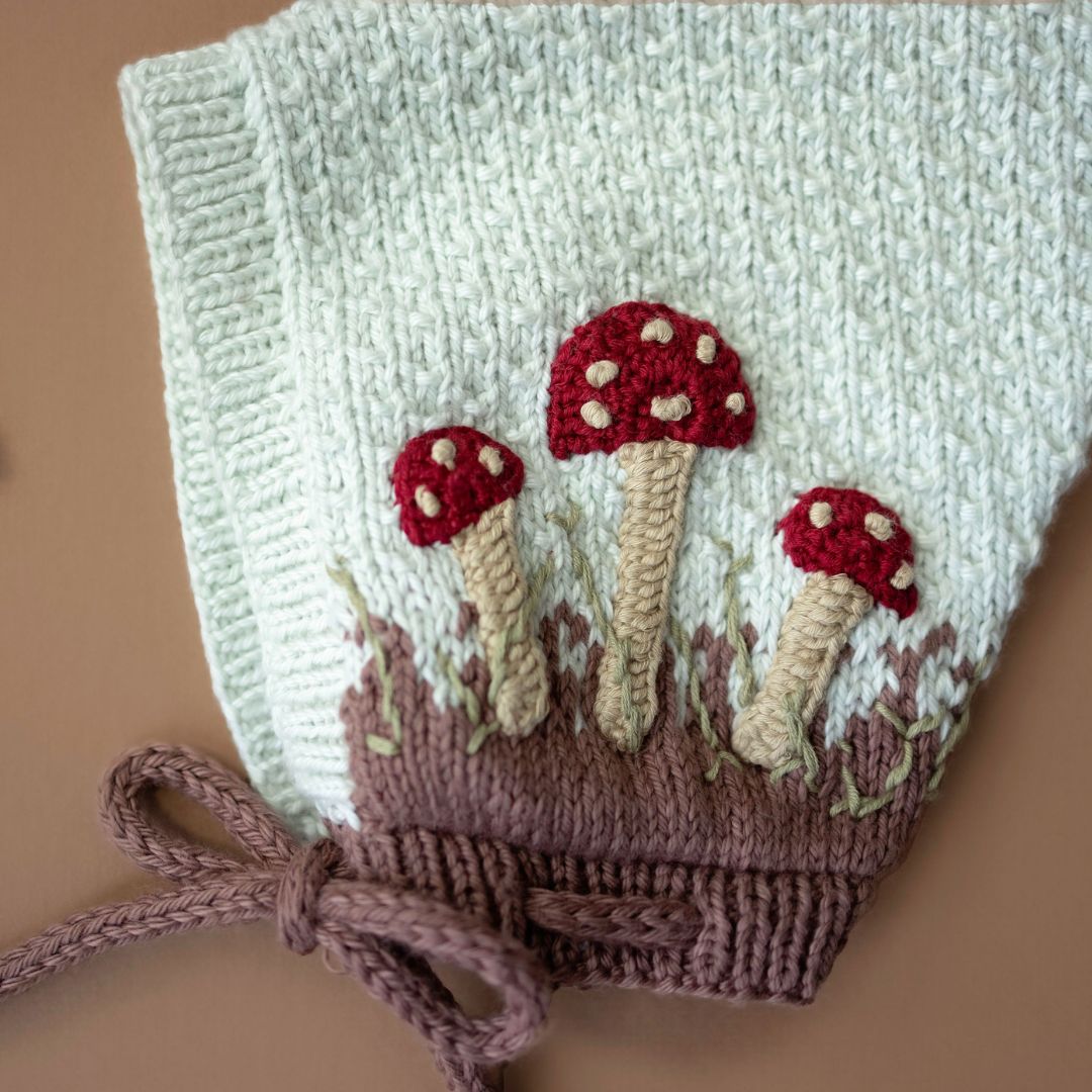 Light green knit pixie hat with red mushroom embroidery, mocha knit cuff and ties