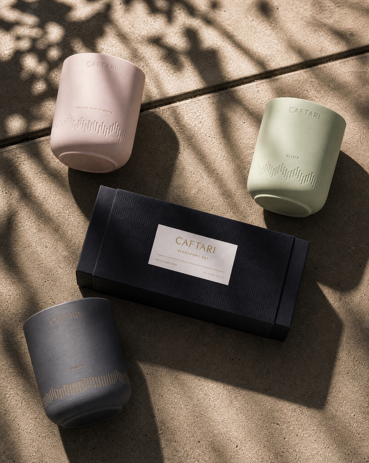 Signature gift set of Caftari candles: pink, sage, and dark gray cups on a navy box