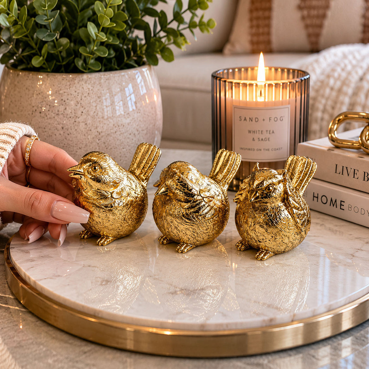 Gold-tone three bird figurines on a round tabletop, hand adjusting the front bird