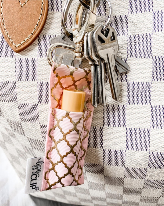 Light pink quatrefoil lip balm holder with gold clip, shown on a key ring