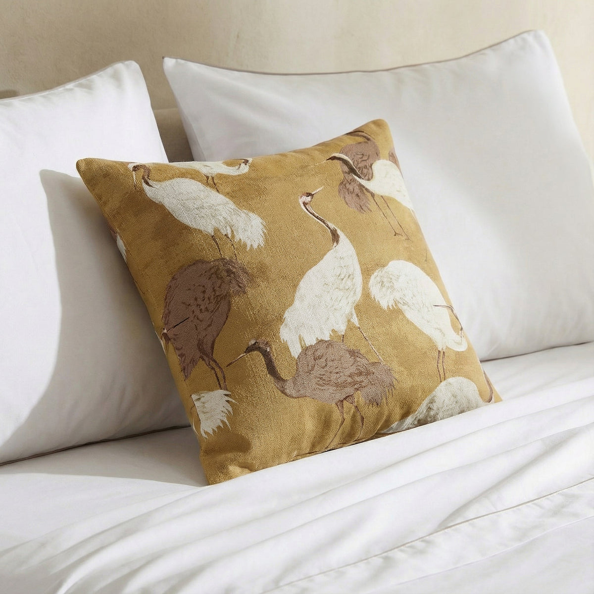 Gold crane throw pillow on white bedding with white, brown, and cream birds