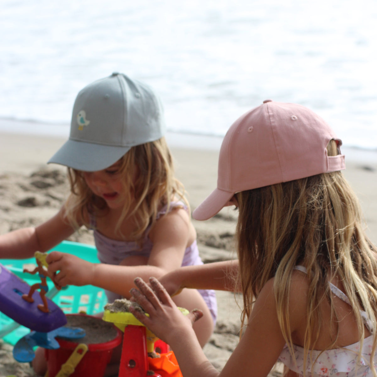Pale blue children's baseball cap with bird patch, shown worn at the beach