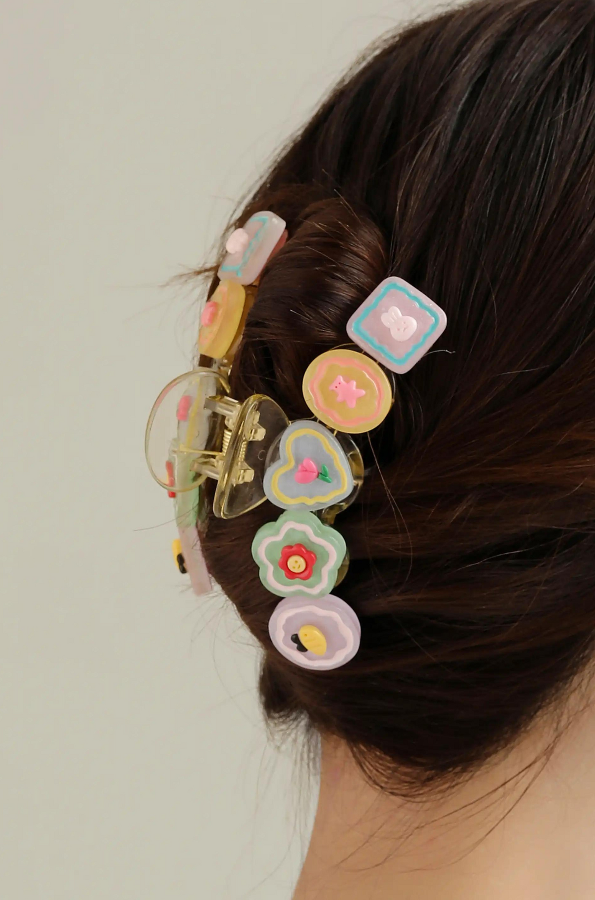 Decorative hair claw with pastel flower and fruit charms, worn in dark hair