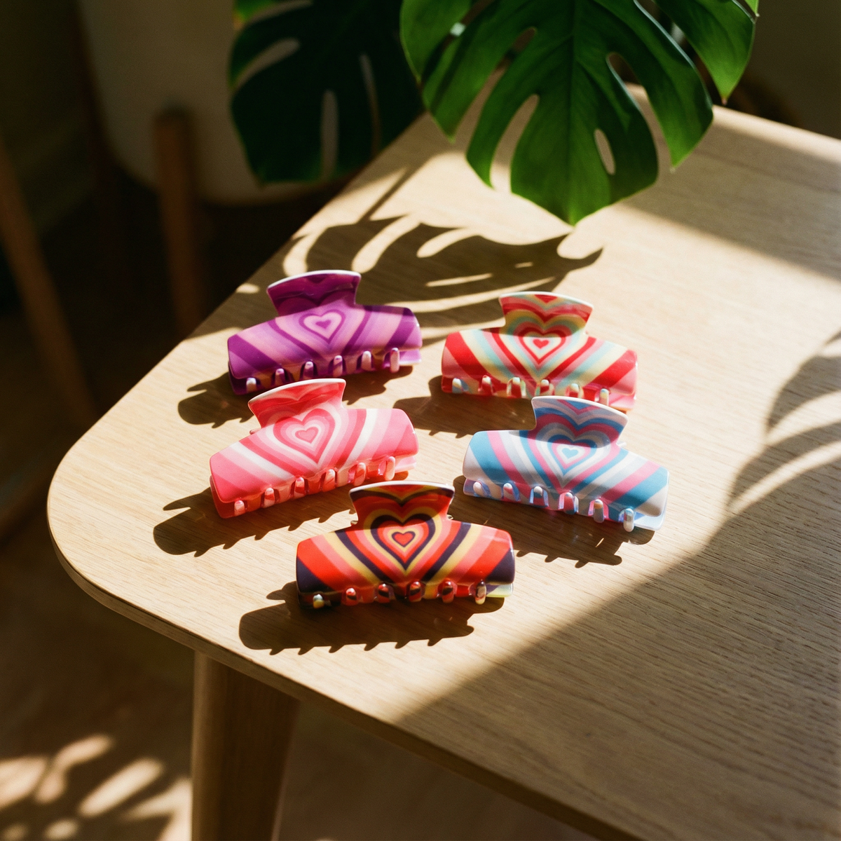 Five colorful heart-pattern hair claw clips on a wooden tabletop