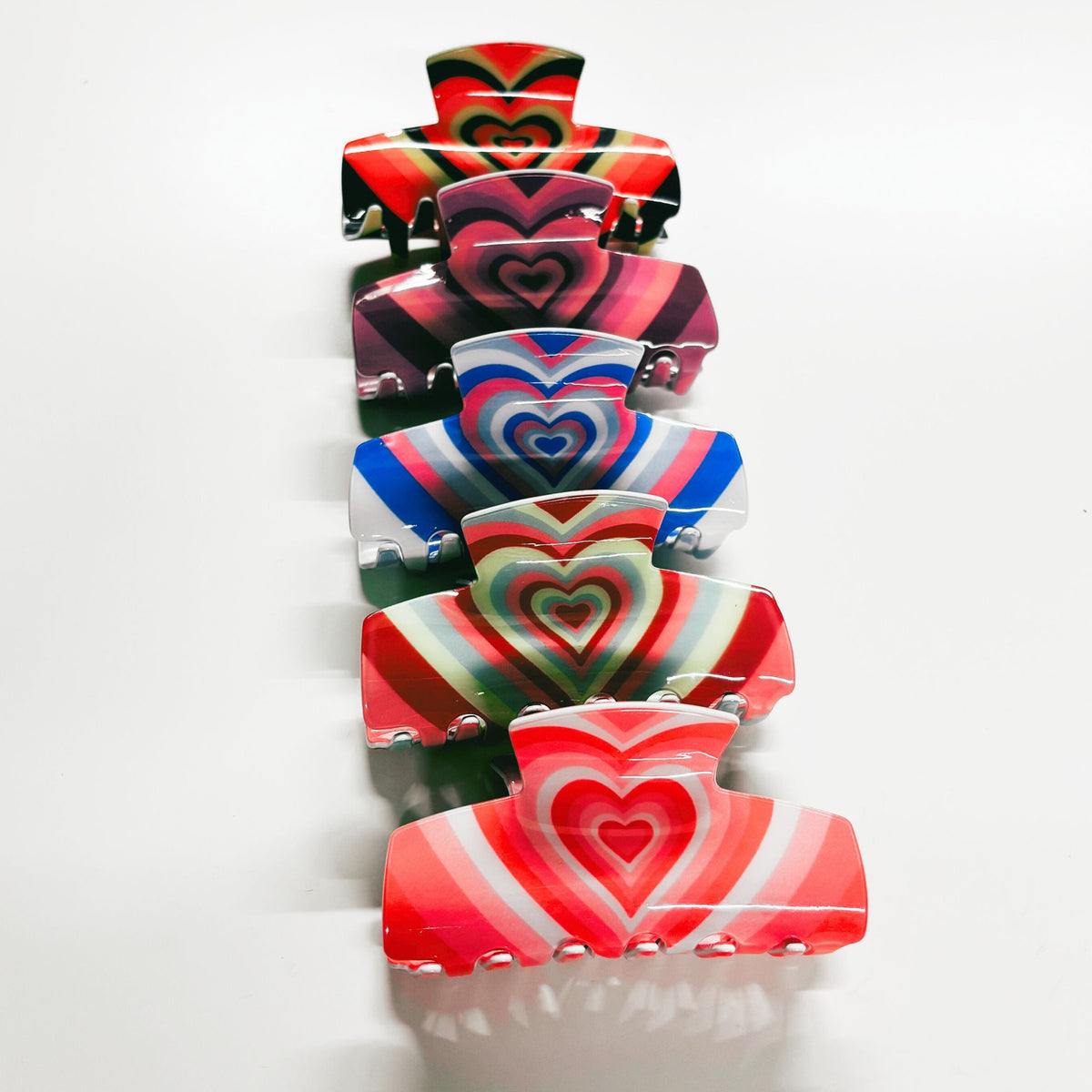 Five heart-striped hair claw clips stacked with red, rainbow, and blue colors
