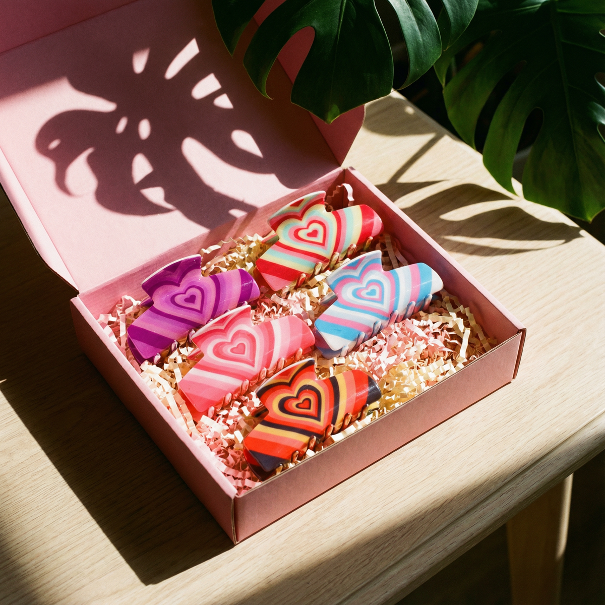 Open gift box with five colorful heart-striped hair claw clips