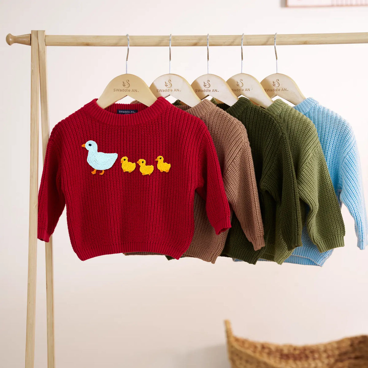 Baby knit duck sweaters hanging on a rack in red, brown, green, and blue colors