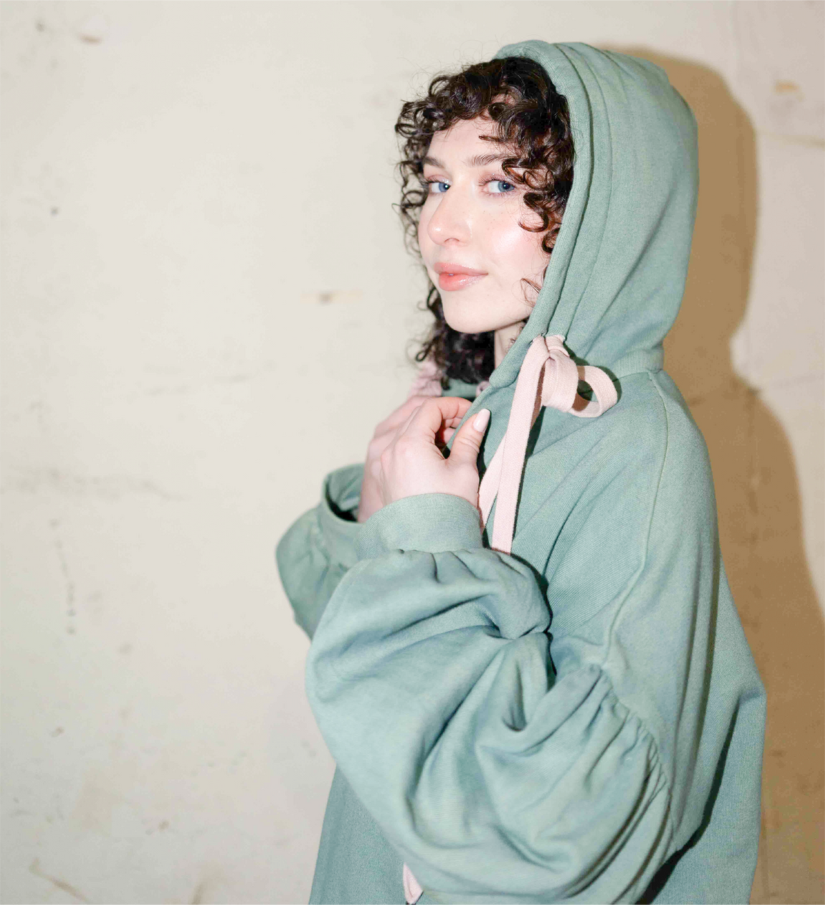 Side view of the hoodie worn with its hood up and pink drawstrings tied at the neck.