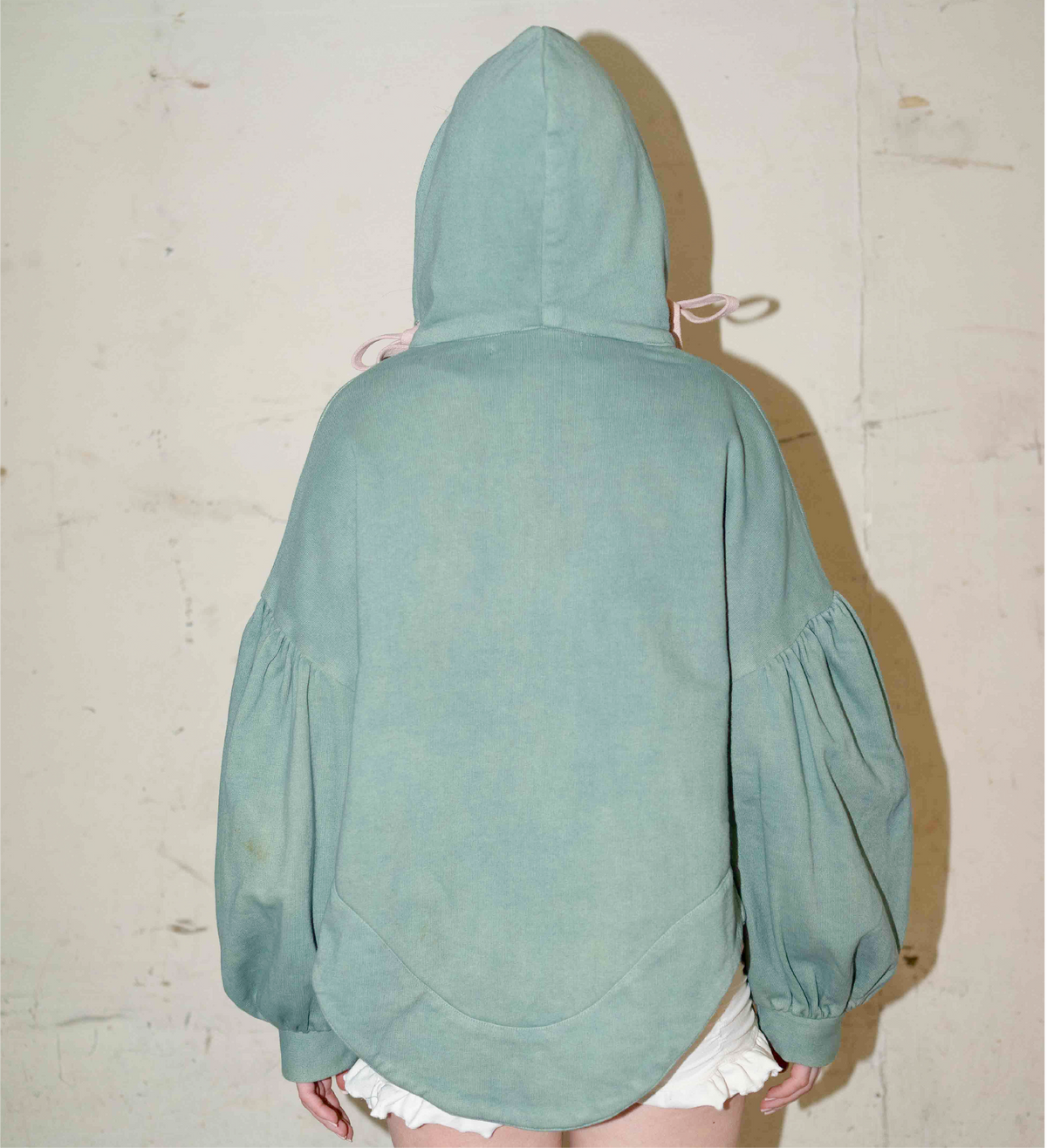 Back view of the sage green hoodie with a rounded hem and voluminous gathered sleeves.