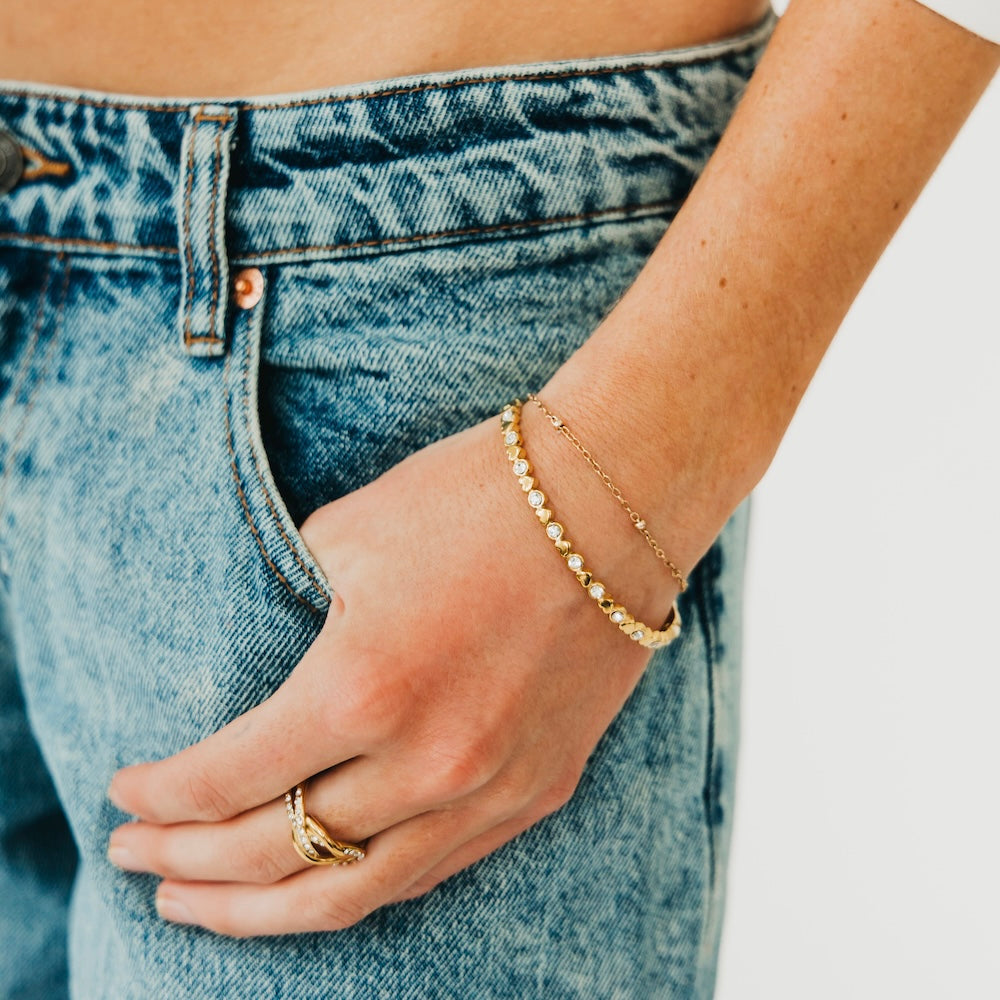 Gold hinge bracelet with heart charms and diamond-like stones on wrist