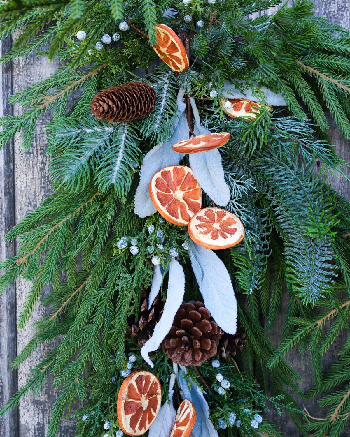 Evergreen garland detail with orange slice ornaments, blue-gray pinecones, and white ribbons