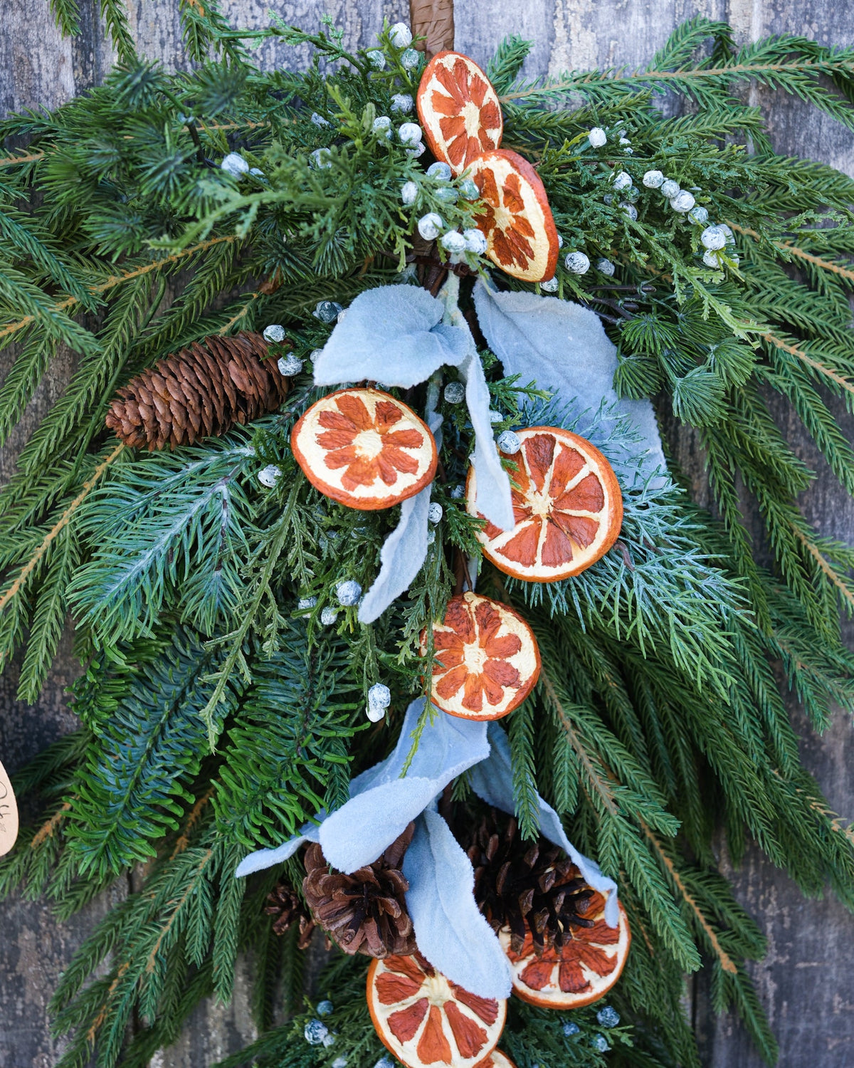 Evergreen garland with orange slice ornaments, pinecones, white ribbon streamers, and berry accents