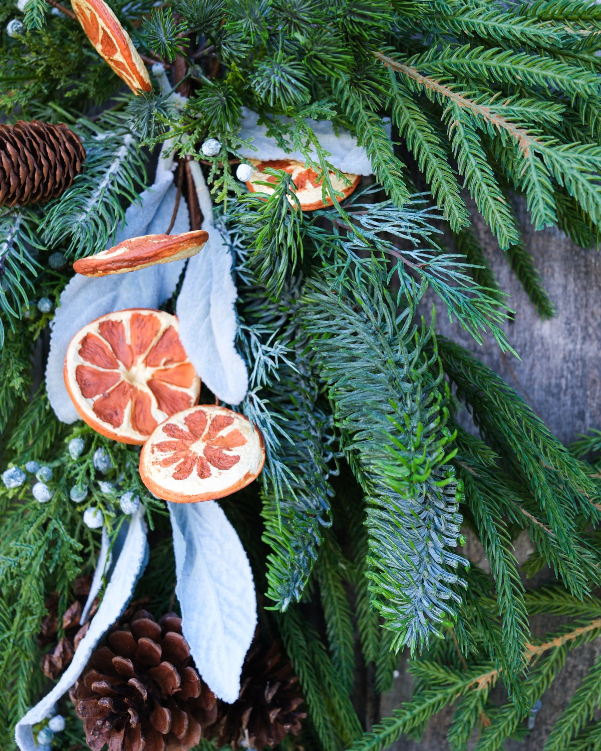 Evergreen garland close-up with orange slice ornaments and pinecones beside white ribbon tails