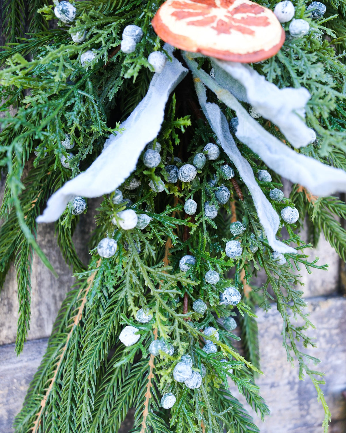 Evergreen garland overhead view with orange slice accents, white ribbons, and frosted bead details