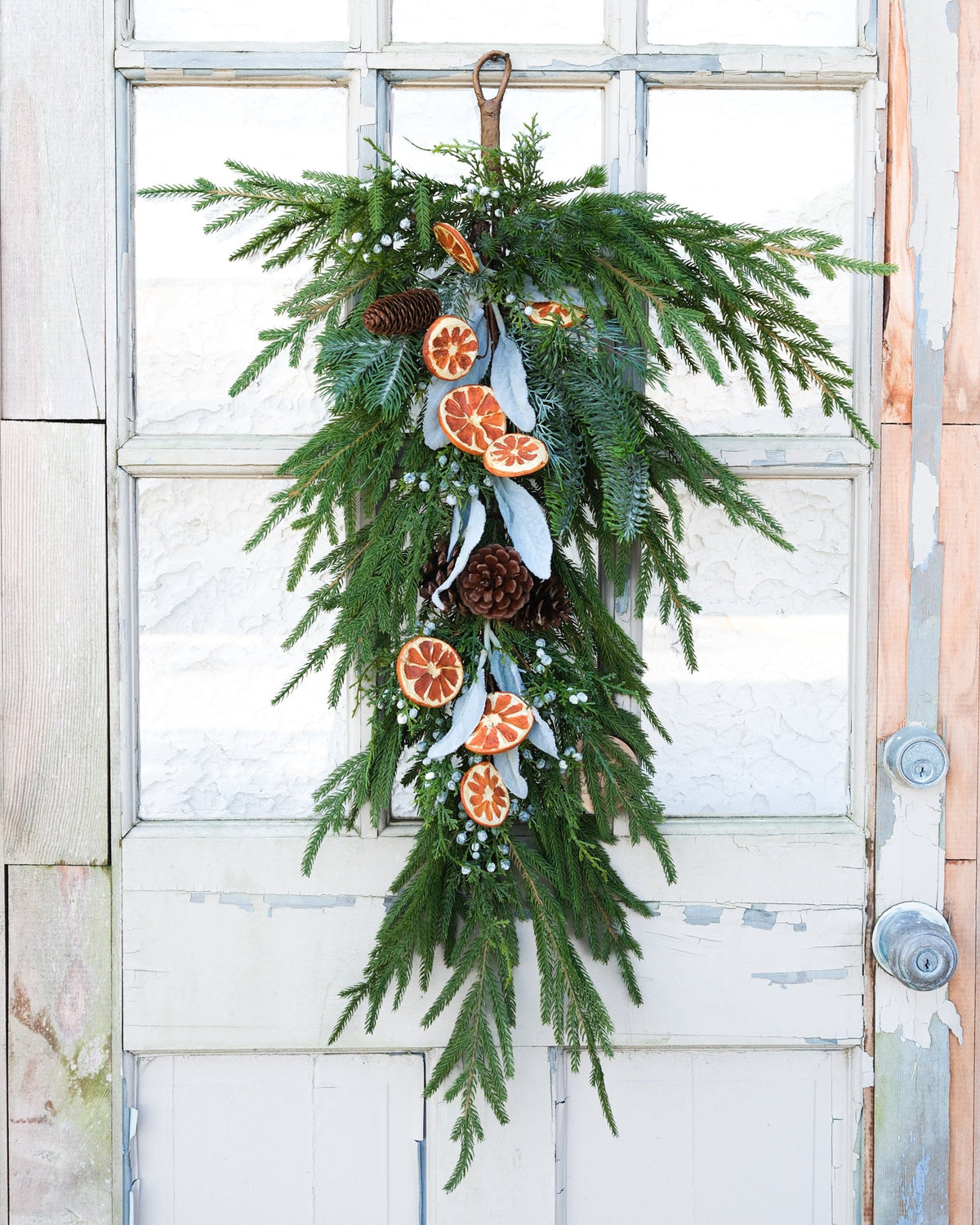 Evergreen holiday drop garland hanging on a white door with orange slice and pinecone ornaments