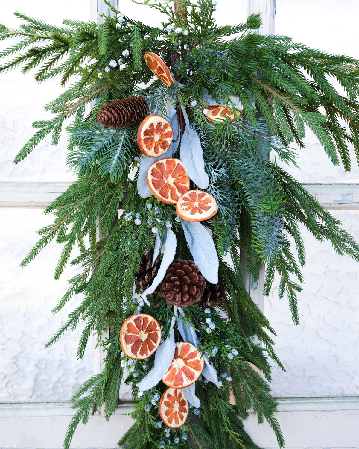Evergreen holiday drop garland with orange slice ornaments, white ribbons, pinecones, and frosted beads