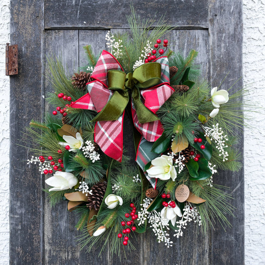 Holiday wreath with green pine branches, white flowers, red berries, and red plaid bow