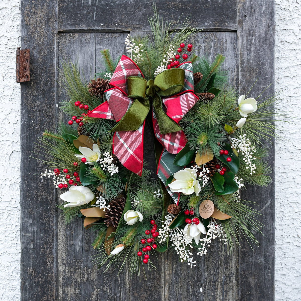 Holiday wreath with red-and-green plaid bow, white flowers, red berries, evergreen greenery