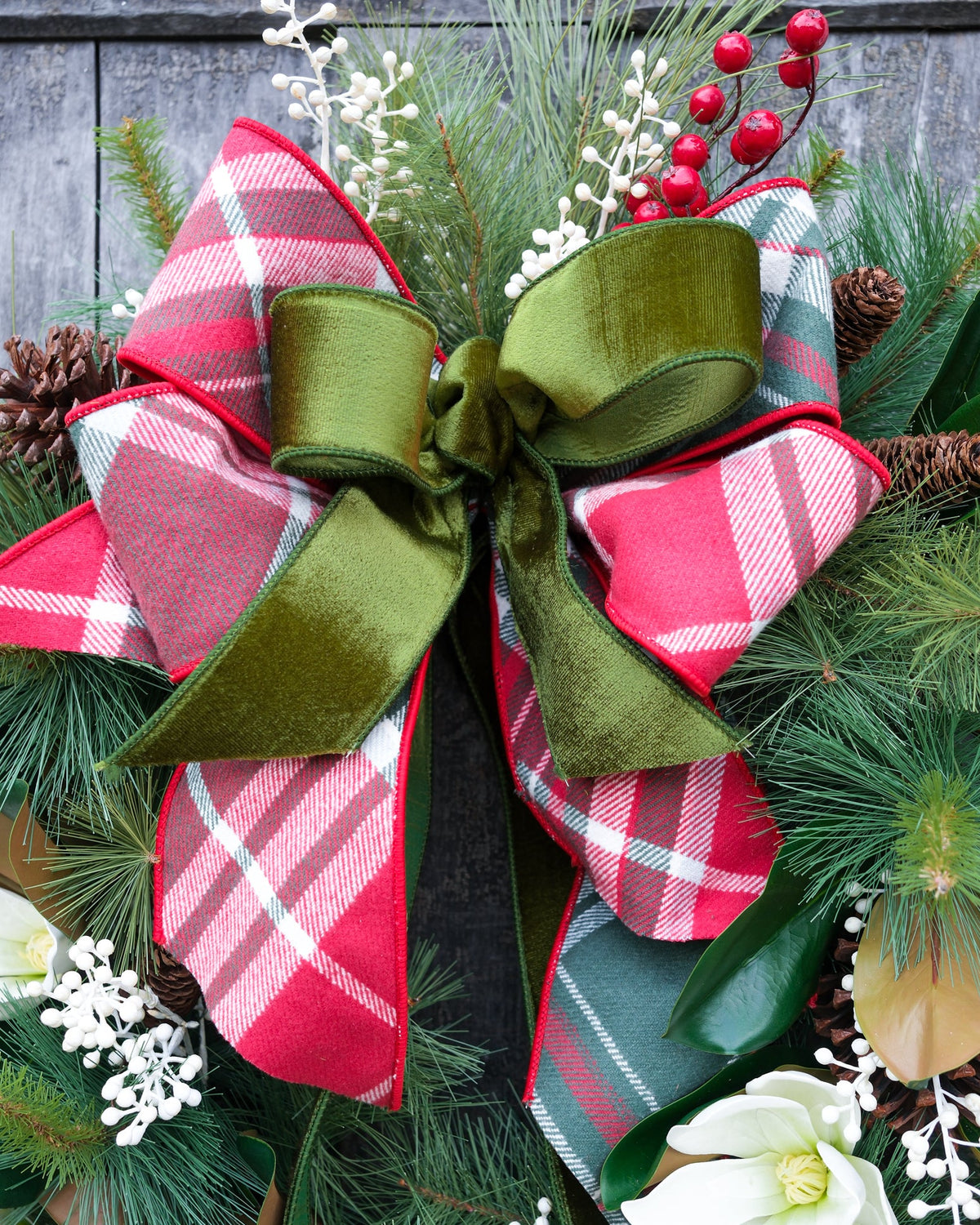 Holiday wreath view with large green-and-red plaid bow and evergreen branches with pinecone
