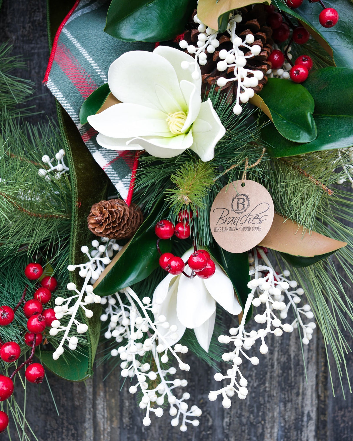 Holiday wreath with white flower accents, green leaves, red berries, and pinecone detail